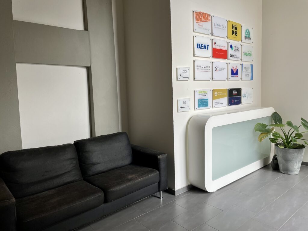 Empfangsbereich des Co-Working-Spaces mit schwarzem Sofa, Theke und Firmenschildern im Kölner Büro